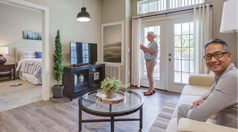 A man and woman are sitting in a living room. The woman is standing and looking at the man. The living room has a couch, a chair, a coffee table, and a television. There are also potted plants and a vase in the room. AI generated content