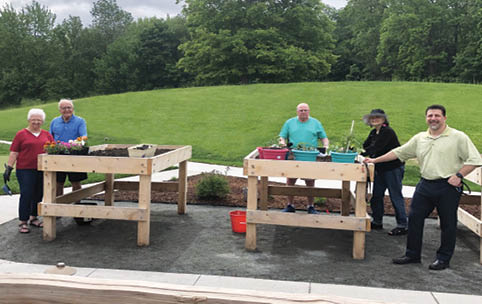 A group of people are standing around a picnic table in a park. AI generated content